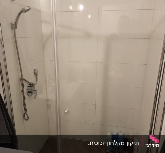 מקלחון זכוכית פינתי מותקן בחדר רחצה עם חיפוי אריחים לבנים